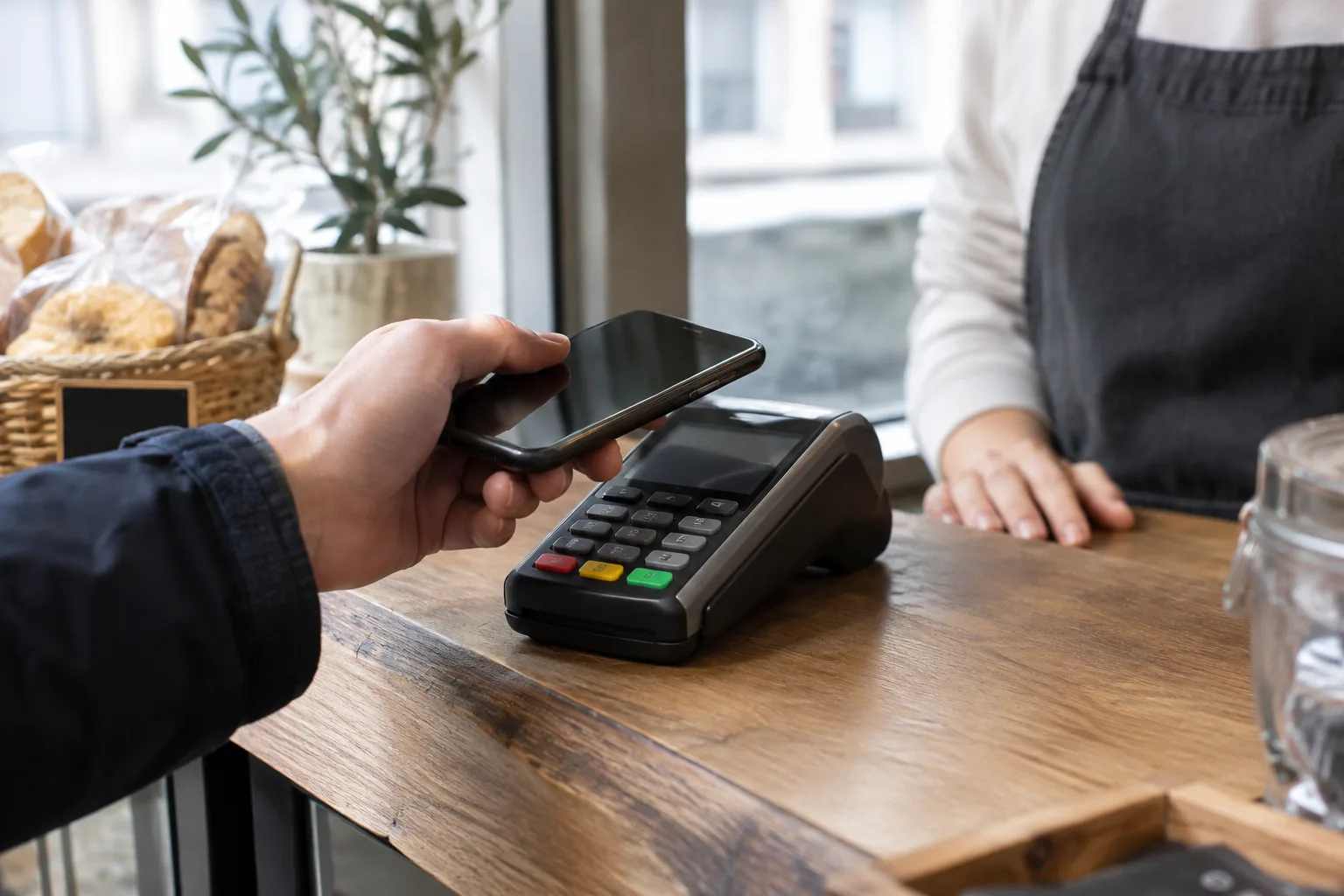 Une personne approche son téléphone d’un terminal de paiement dans un commerce.